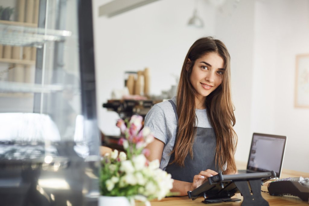 Coffee shop owner using a tablet looking at camera smiling, waiting for her first customer