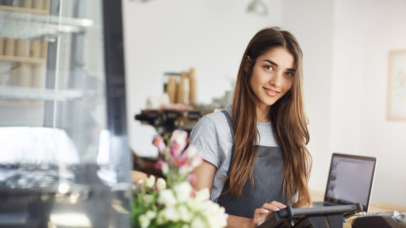 Coffee shop owner using a tablet looking at camera smiling, waiting for her first customer